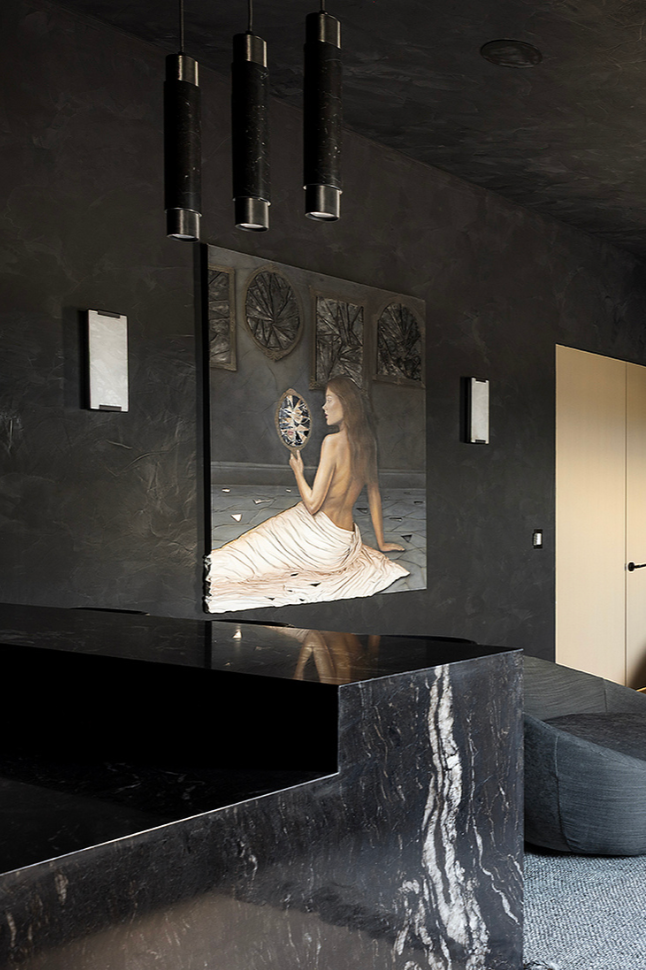 An interior room with dark gray textured walls, modern black pendant lights hanging from the ceiling, and a large painting of a woman holding a mirror, seated on the floor with a draped cloth.