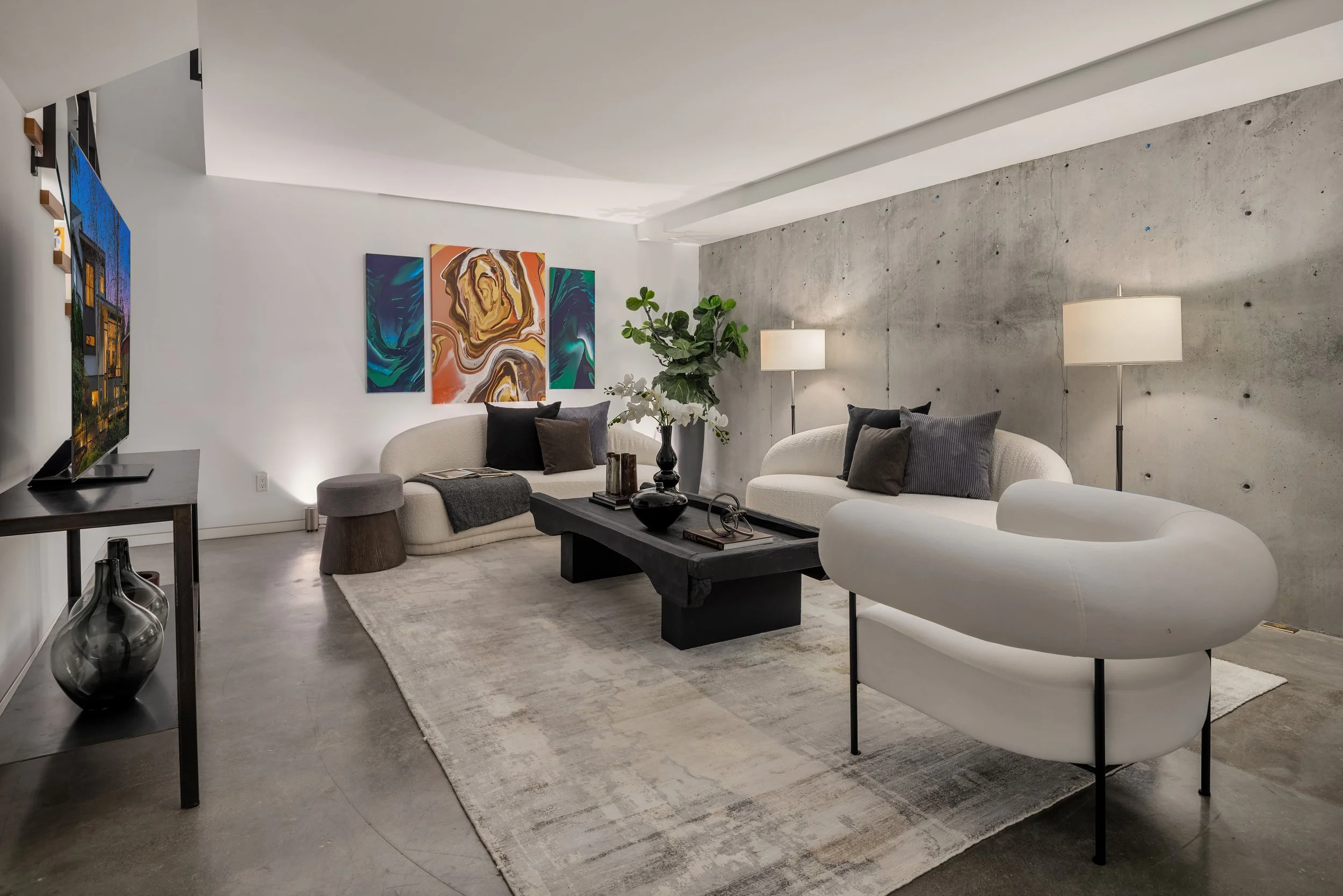 Open-concept living room and kitchen with modern decor, colorful paintings, green and orange sofas, and pendant lights over kitchen island with bar stools.