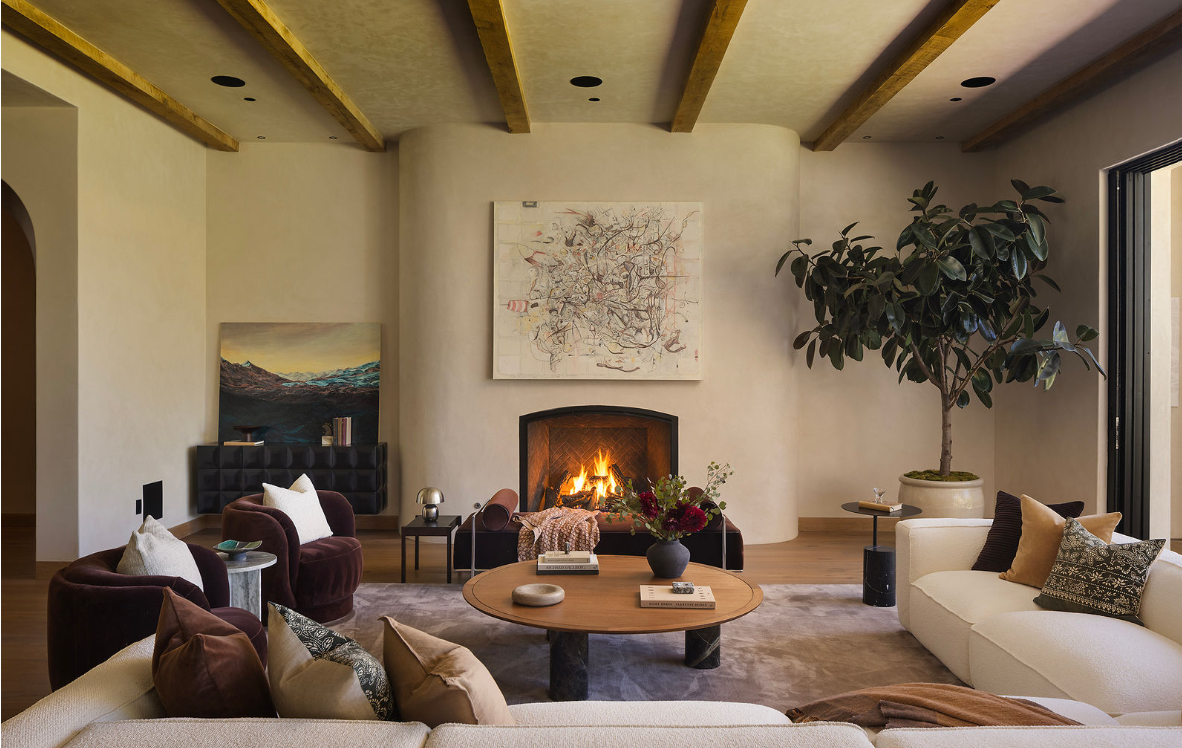 Living room with beige walls, wooden ceiling, colorful wall art, green and coral sofas, coffee table with plants, and a bar area with stools.