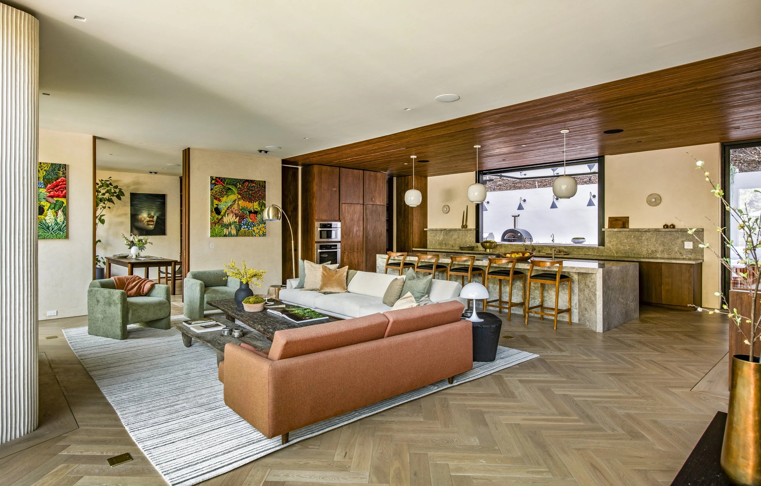 Open concept living room and kitchen with modern furniture, artwork, and large windows letting in natural light.