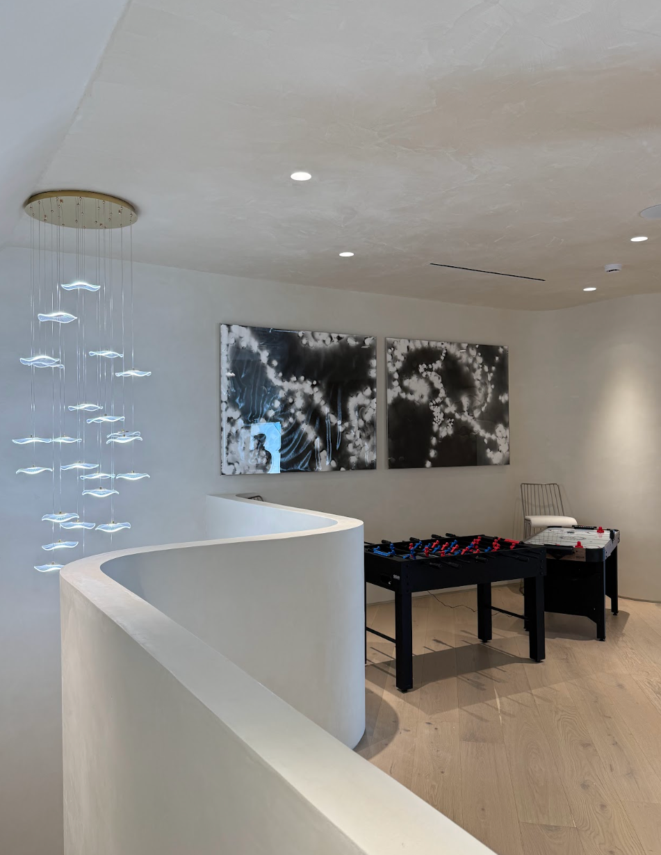 Modern interior room with white curved wall, abstract black and white artwork, foosball table, and decorative hanging light. Luxury art staging in Los Angeles featuring museum-quality contemporary artwork in a modern luxury residence.