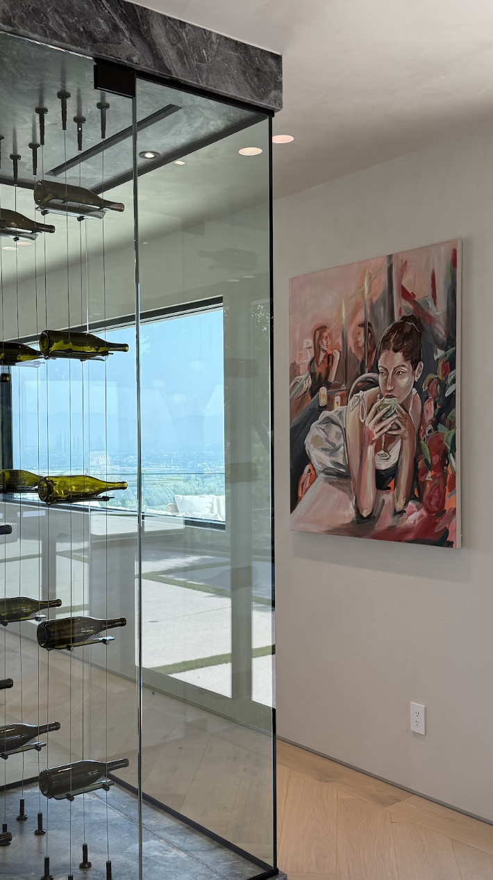 Luxury art staging in Los Angeles featuring museum-quality contemporary artwork in a modern luxury resTo the right, a colorful painting of a woman drinking, situated on a white wall. Large window offering a cityscape view with a clear blue sky Luxury