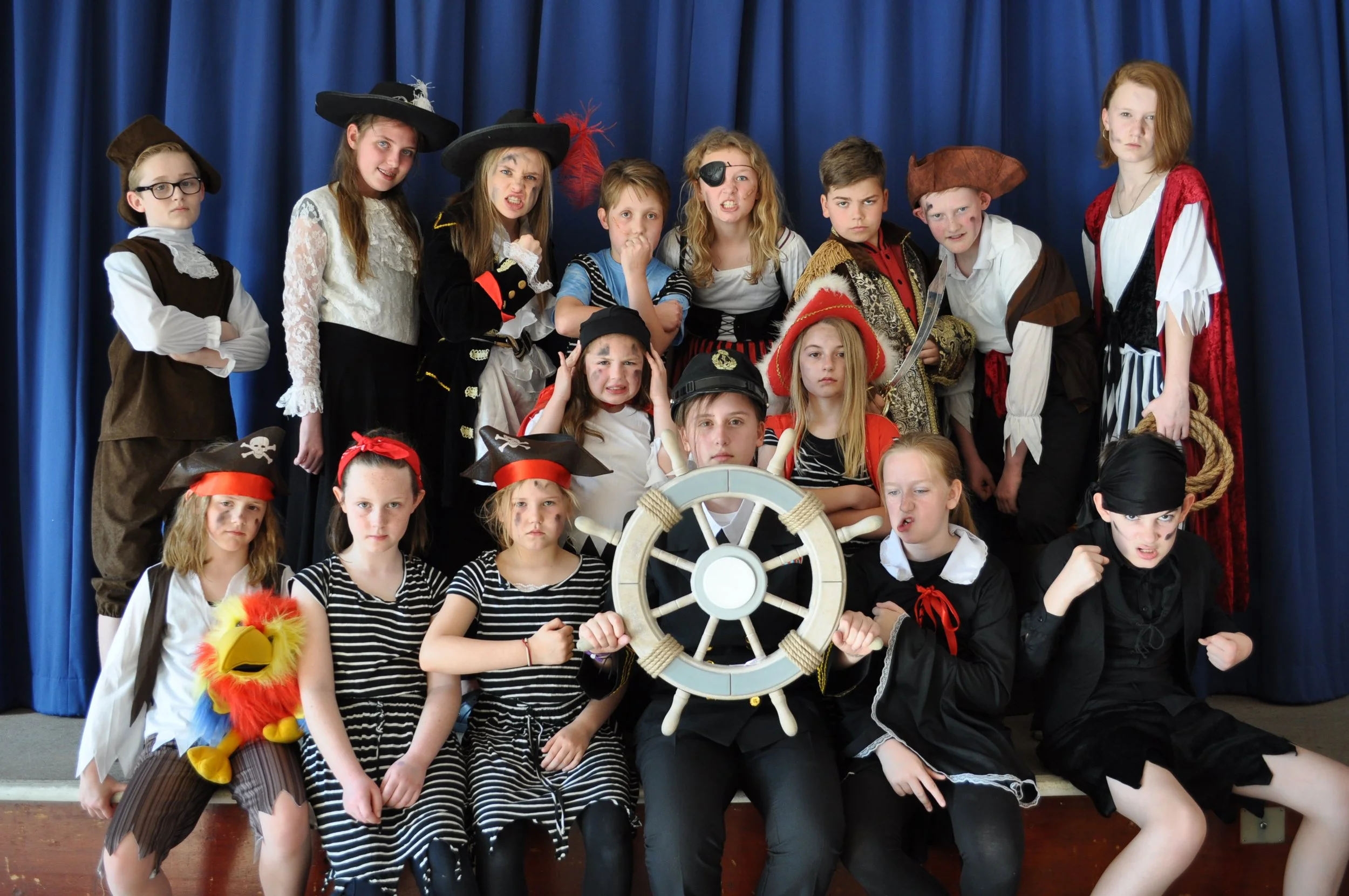 Children dressed as pirates and a sailor, some displaying angry or serious expressions, on stage with a blue curtain background.