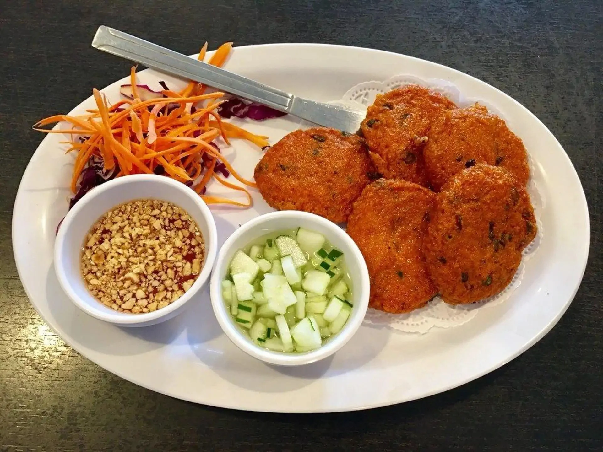 Plate of Vietnamese banh mi with breaded fish fillets, shredded carrots, and side dishes of chopped cucumber in vinegar, crushed peanuts in sauce, and shredded purple cabbage with a dipping sauce.