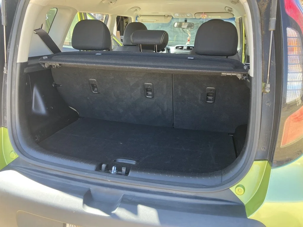 The rear trunk of a green SUV or crossover vehicle with the cargo area open, showing an empty space with black interior lining and the back of the rear seats.
