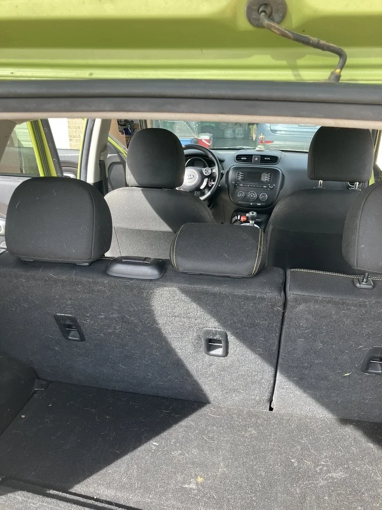 View of the interior of a green hatchback car, showing the back seats and cargo area with the rear hatch open, revealing the dashboard and front seats.