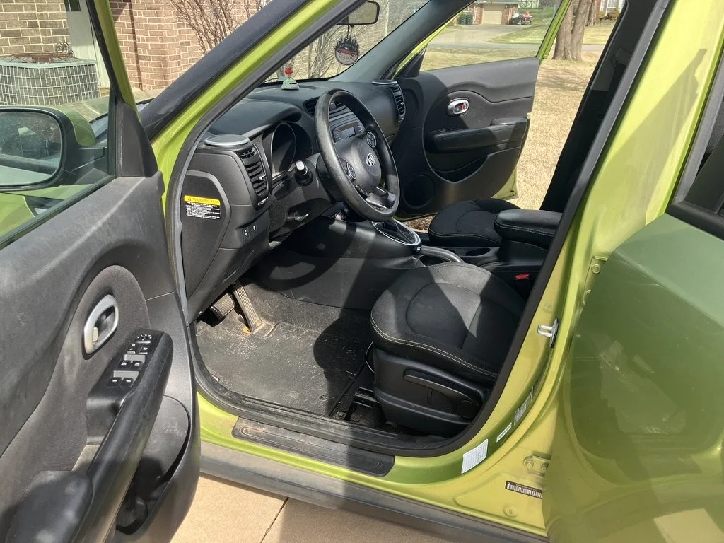 The interior of a lime green compact car, showing the driver's side door open, black seats, and dashboard with steering wheel.