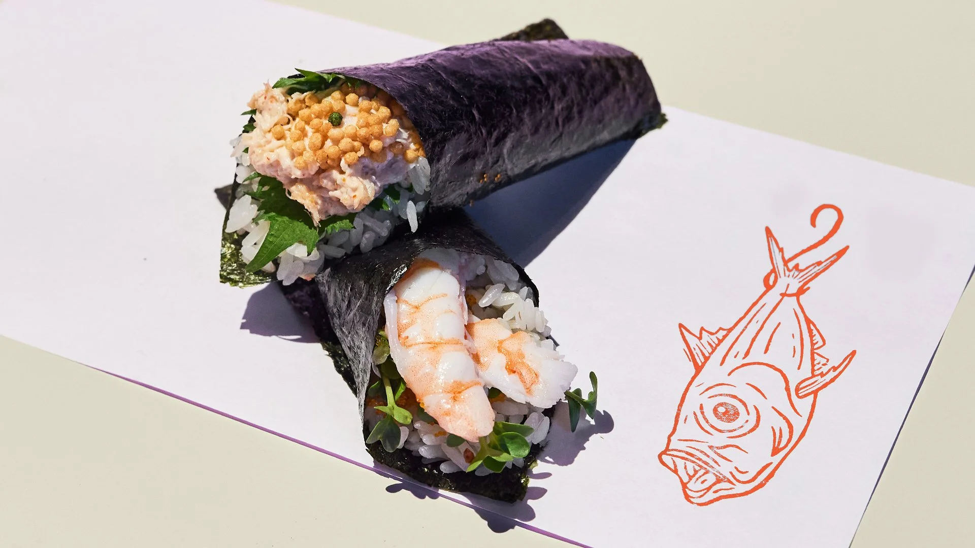 Two temaki (handrolls) on white paper with the Uoichiba Kinmedai illustration.