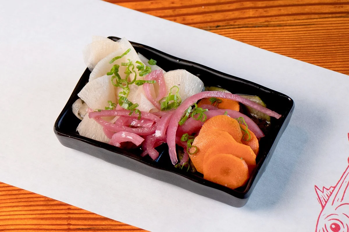 Wood table with white paper place mat with  bowl containing pickled vegetables topped with sliced scallions