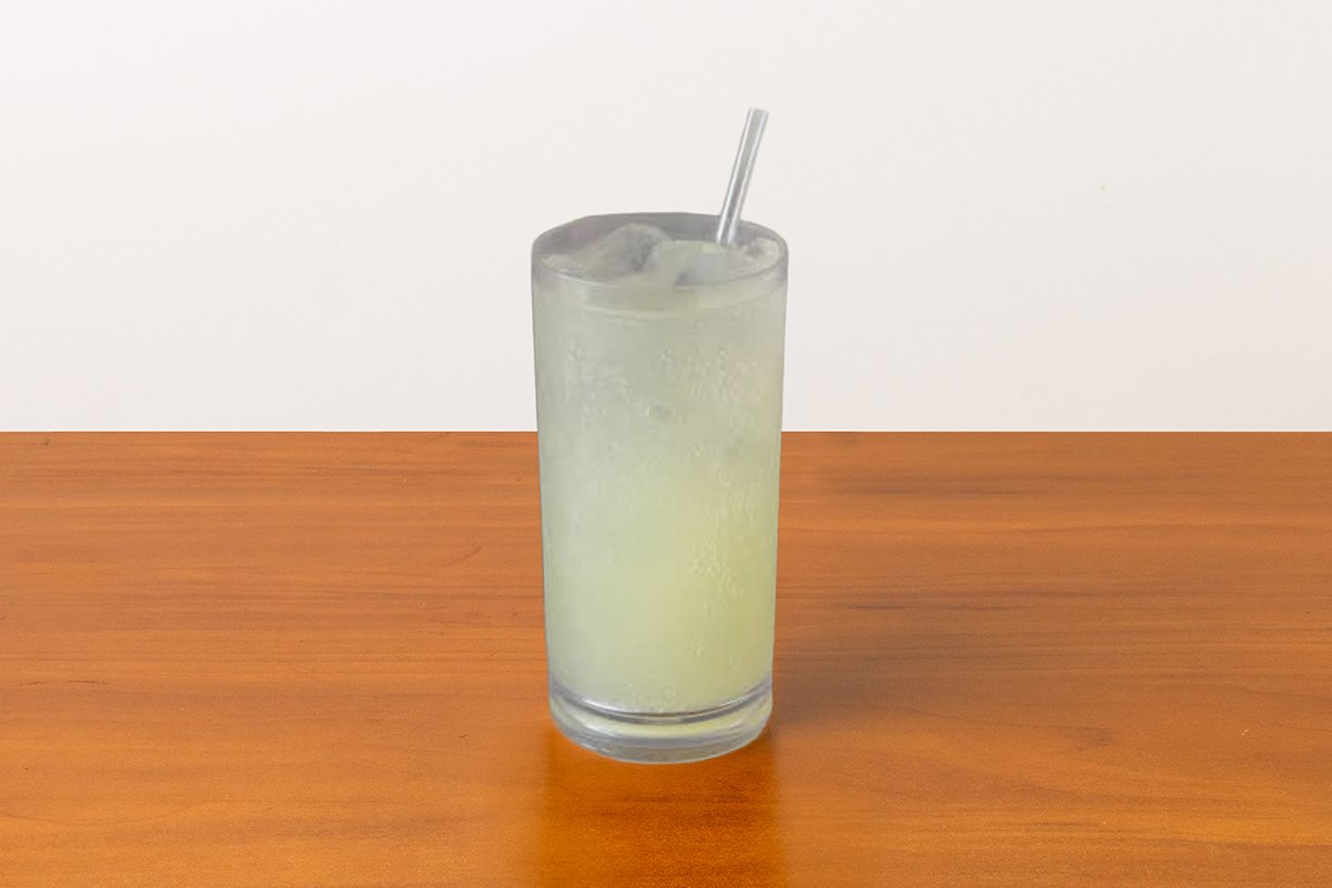 A tall glass of a sparkling yuzu beverage with ice and a straw on a wooden table.