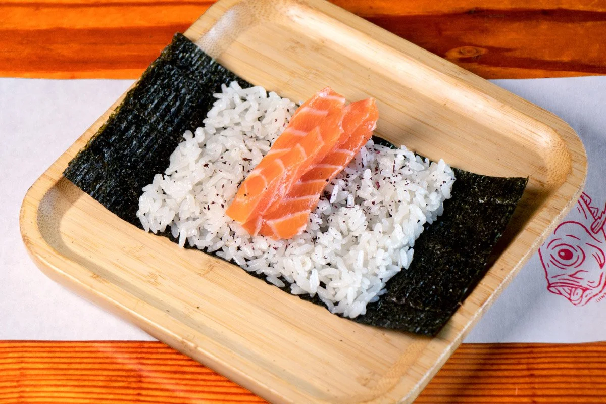 A bamboo tray showcasing an open handroll with steelhead on rice and seaweed.