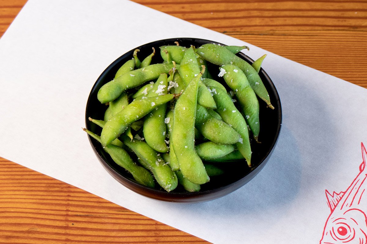 Wood table with white paper place mat with bowl containing edamame topped with salt