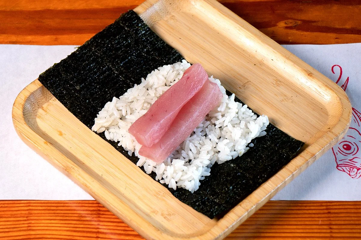 A bamboo tray showcasing an open handroll with lean tuna on rice and seaweed.