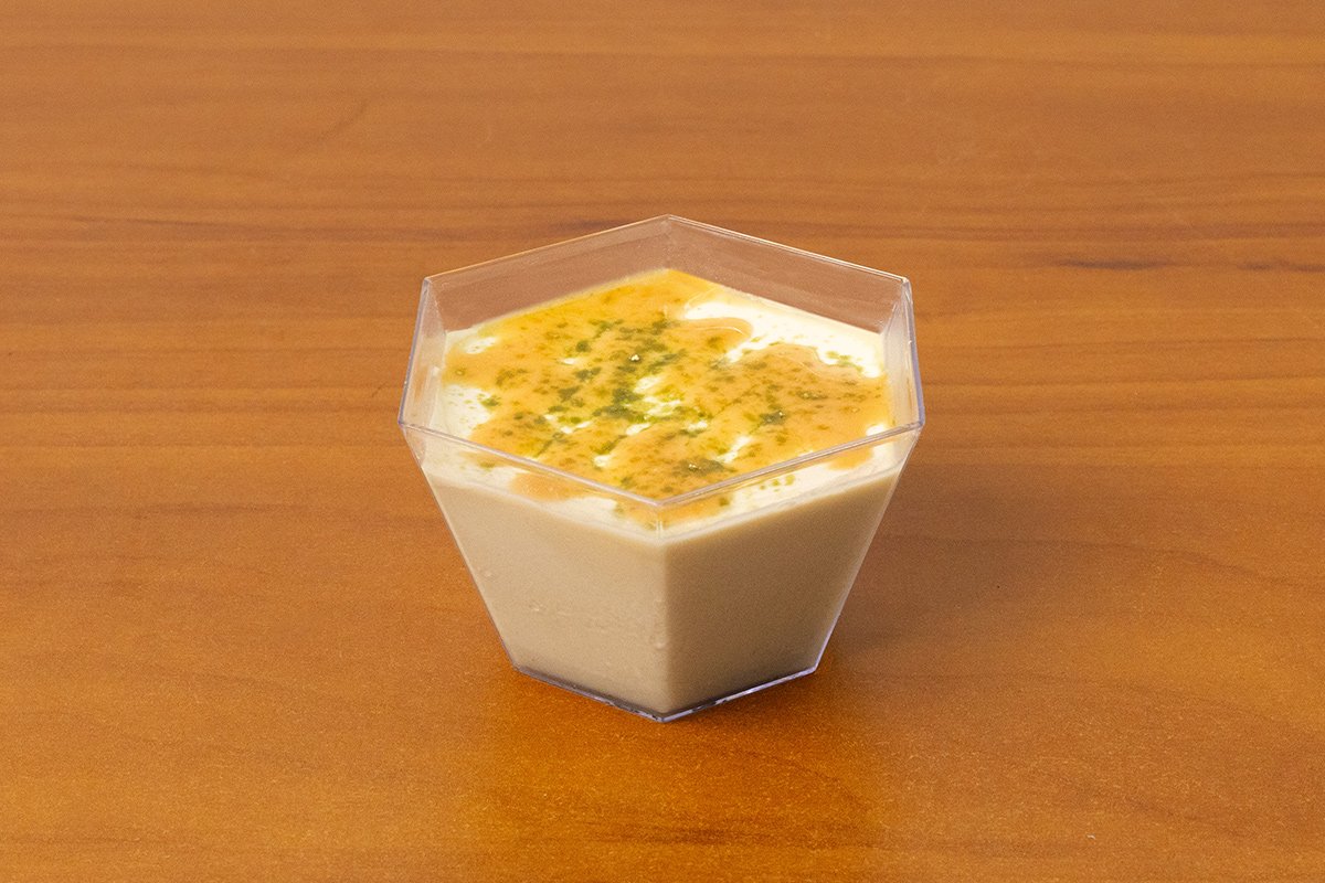 A hexagonal clear container filled with a layered matcha panna cotta dessert, topped with powdered matcha on a wooden surface.