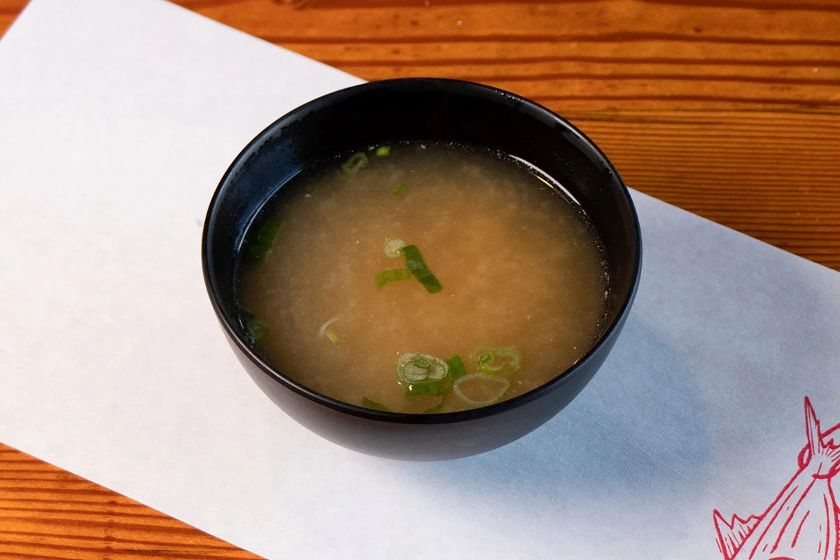 Wood table with white paper place mat with soup bowl containing fish bone stock miso soup