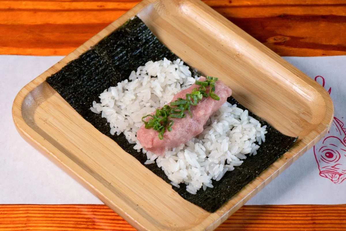 A bamboo tray showcasing an open handroll with fatty bluefin tuna, scallions, on rice and seaweed.