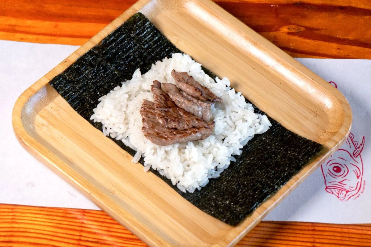 A bamboo tray showcasing an open handroll with torched a5 Japanese wagyu and Maldon salt on rice (shari) and seaweed (nori).