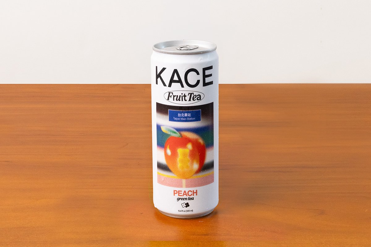 A can of KACE Peach Green Tea Fruit Tea on a wooden surface.