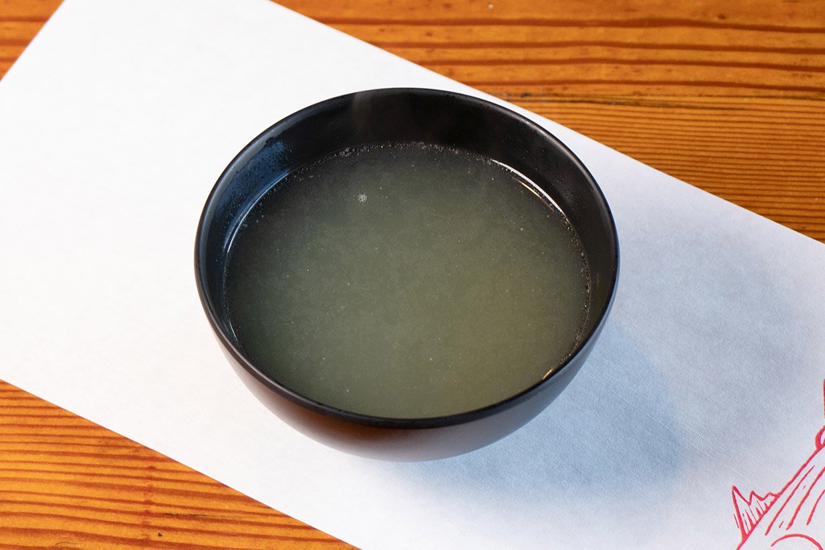 Wood table with white paper place mat with soup bowl containing fish bone stock