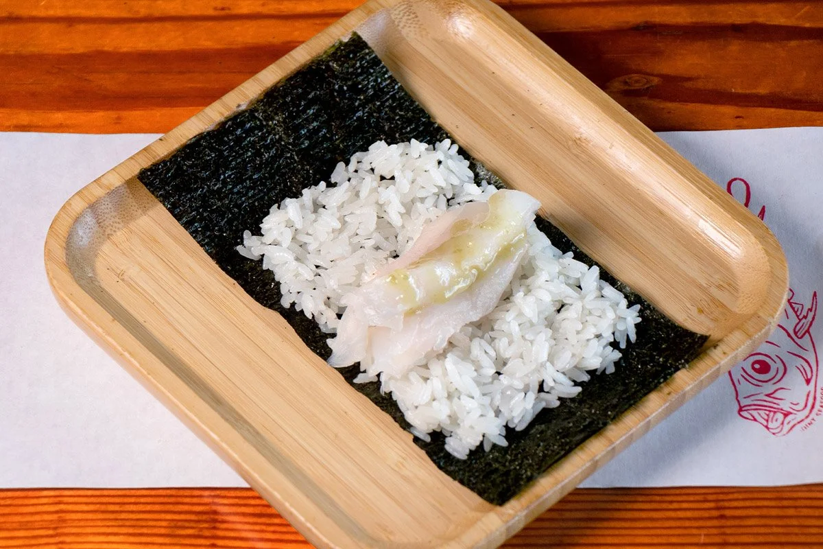 A bamboo tray showcasing an open handroll with whitefish (amberjack/snapper), yuzu it, on rice (shari) and seaweed (nori).