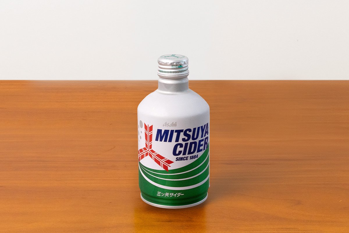 A white bottle of Mitsuya Cider with a silver cap sitting on a wooden surface.