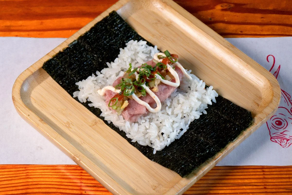 A bamboo tray showcasing an open handroll with fatty tuna, hot yuzu, mayo, scallions and chirashi mix on on rice (shari) and seaweed (nori).