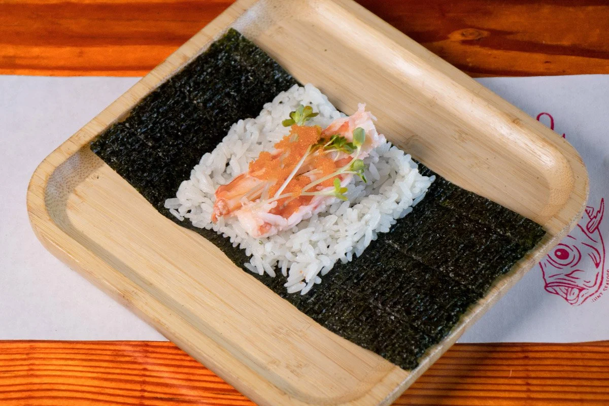 A bamboo tray showcasing an open handroll with poached gari marinated prawn, with daikon sprouts and masago, on rice (shari) and seaweed (nori).