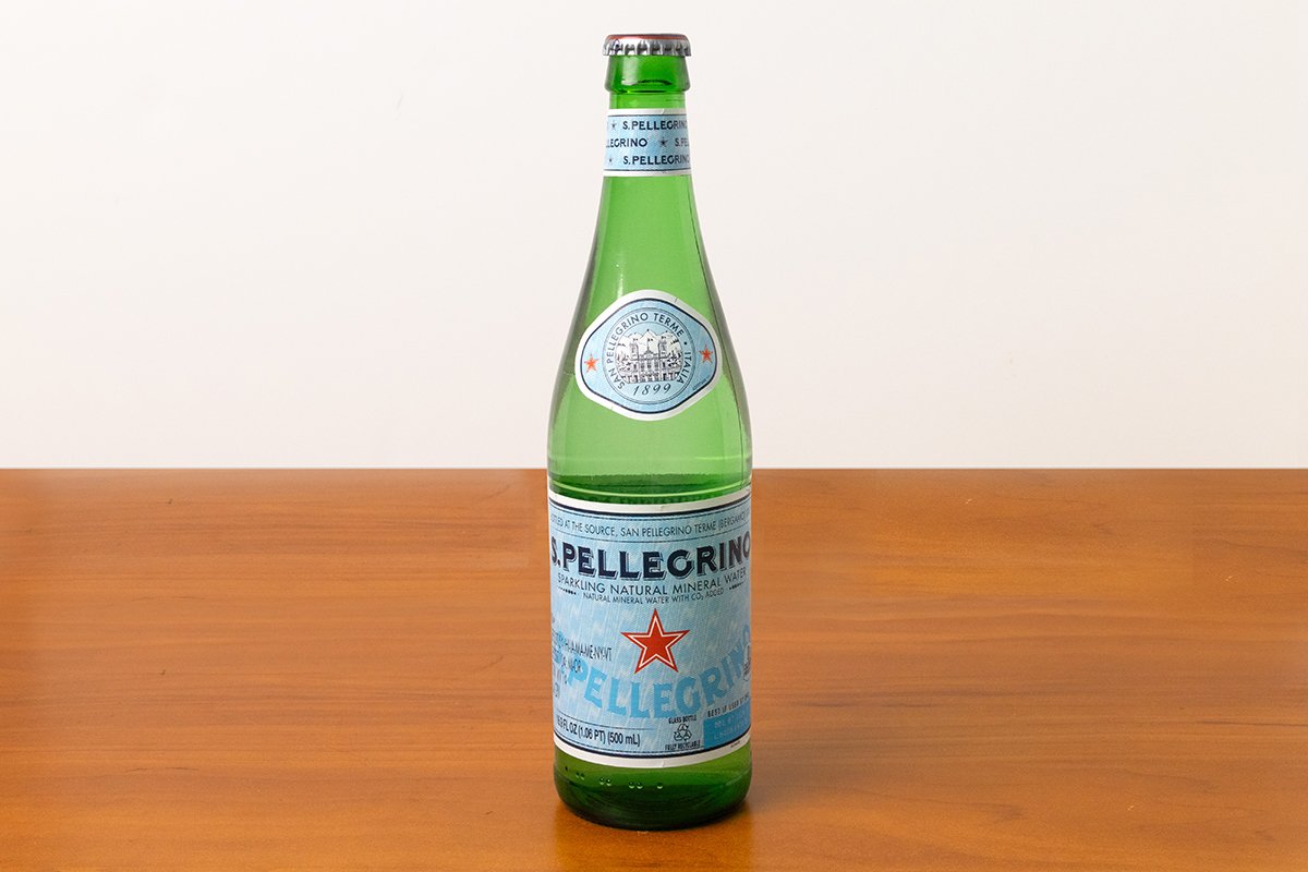A green glass bottle of San Pellegrino sparkling natural mineral water on a wooden surface.