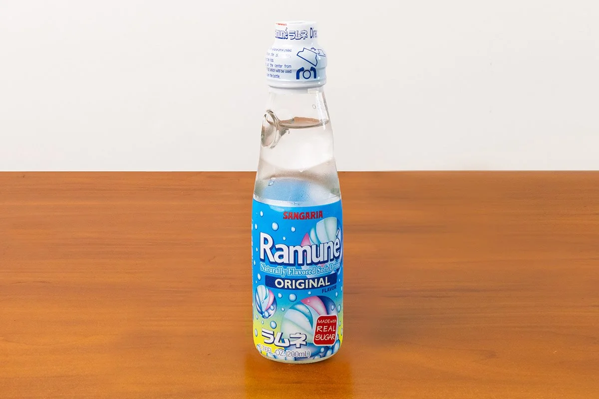 Bottle of Ramune soda with a white cap, placed on a wooden surface.