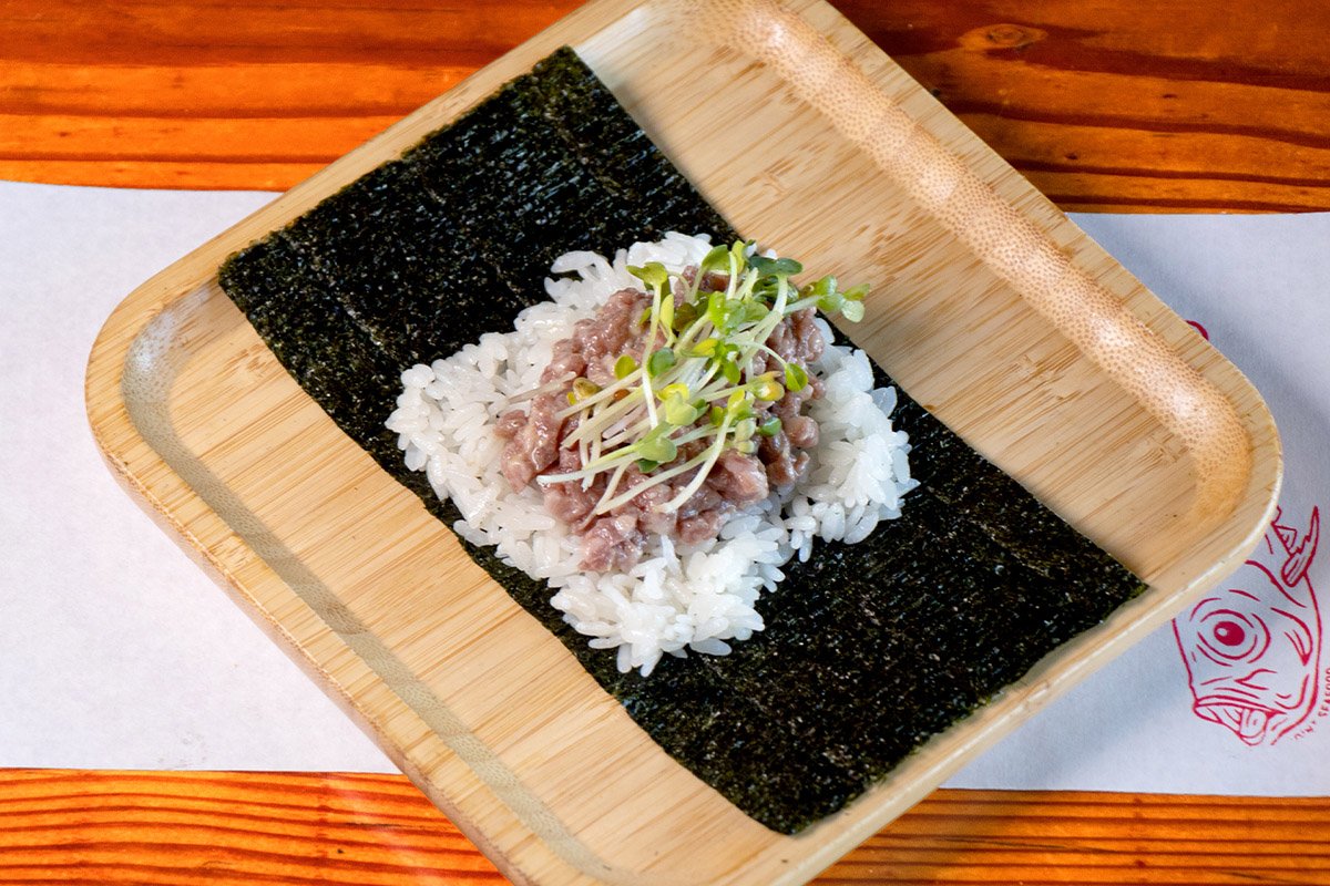 A bamboo tray showcasing an open handroll with Japanese a5 wagyu, daikon sprouts, hot mustard, evoo and maldon on rice (shari) and seaweed (nori).