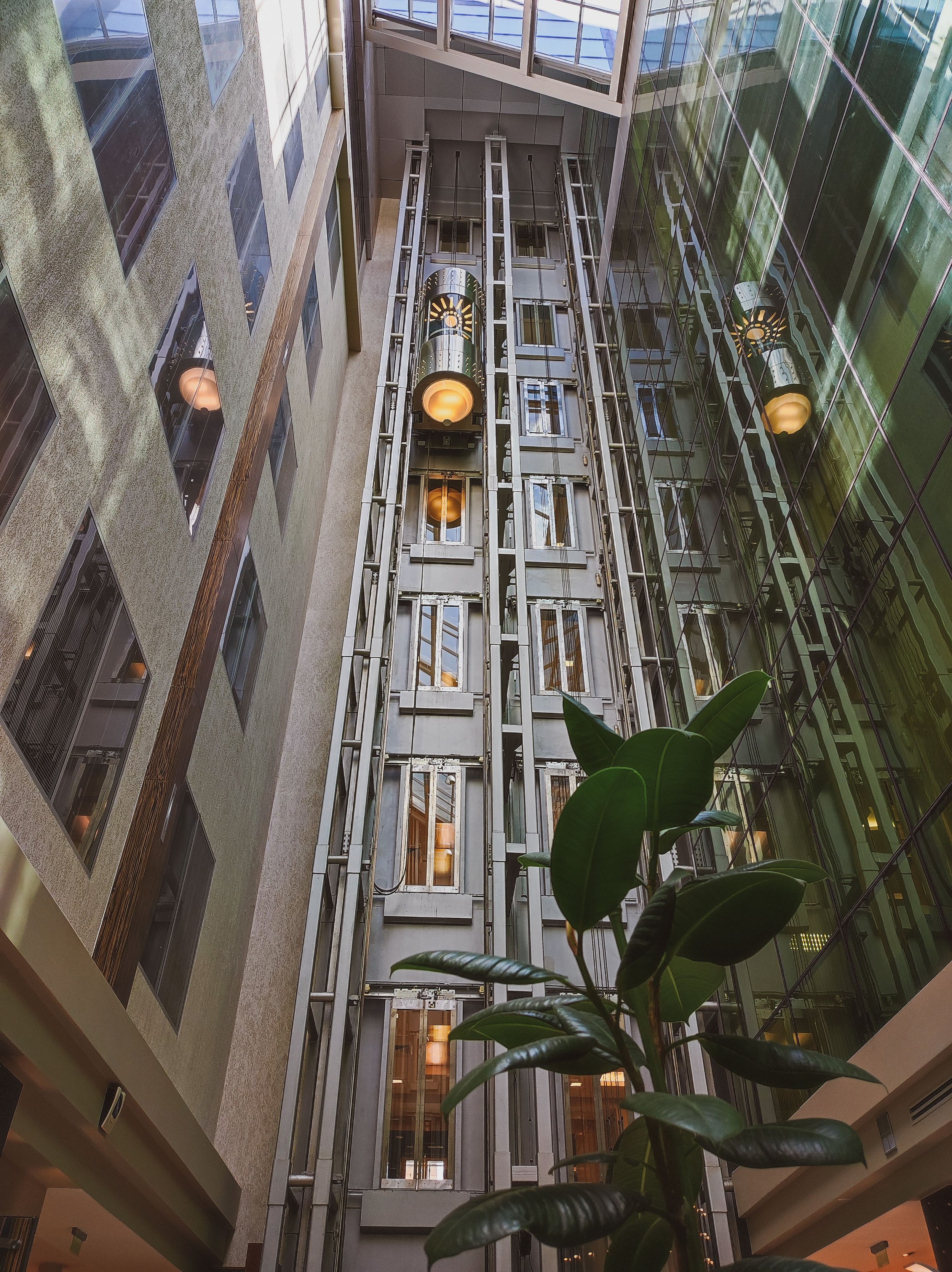 A modern lobby, with an capsule-style elevator traveling upwards along one wall