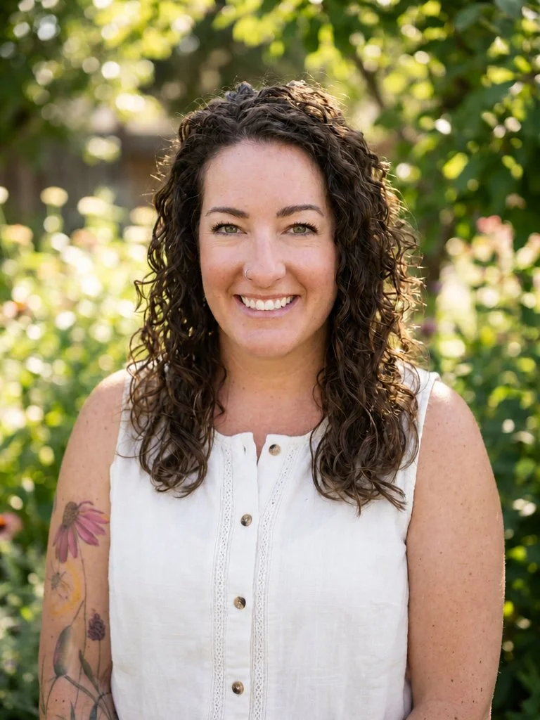 Hannah Dudley is a therapist for grief, trauma, and relationships and is pictured smiling outdoors, wearing a white sleeveless top and showing a colorful floral tattoo on her arm.