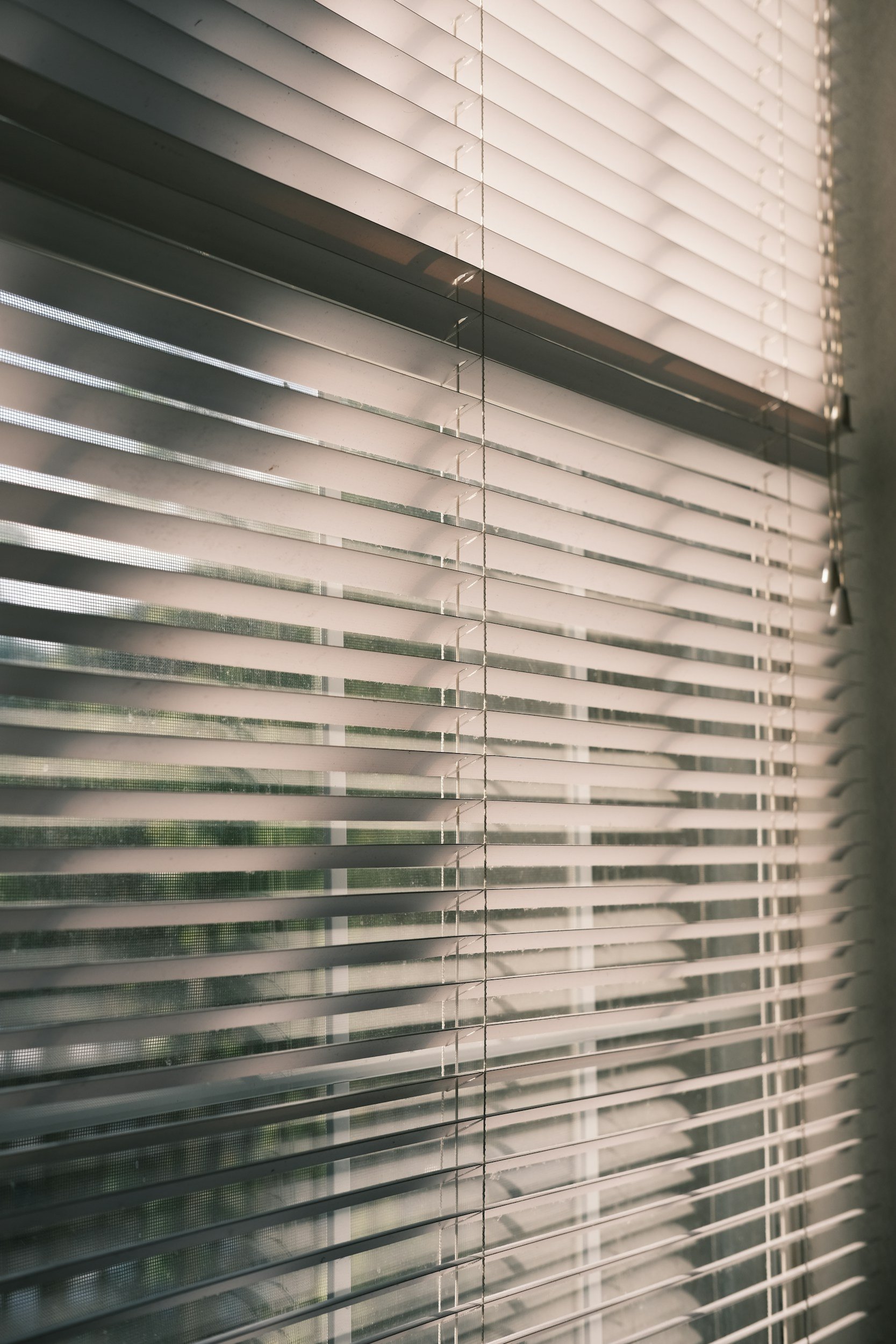 Close-up view of white horizontal window blinds partially open, letting in some light.