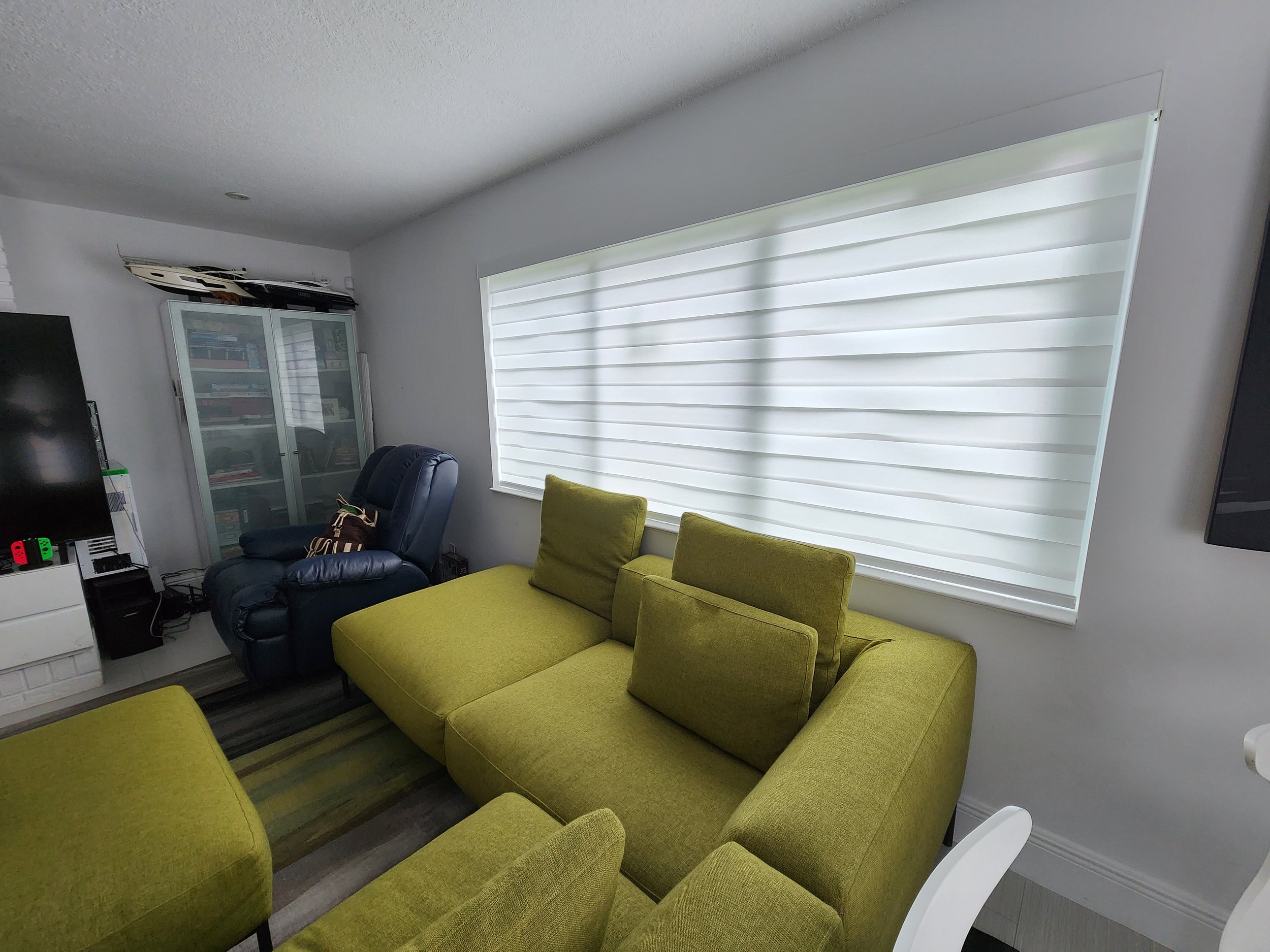 A living room with a large window that has closed battery powered zebra roller blinds for privacy and light filtering.