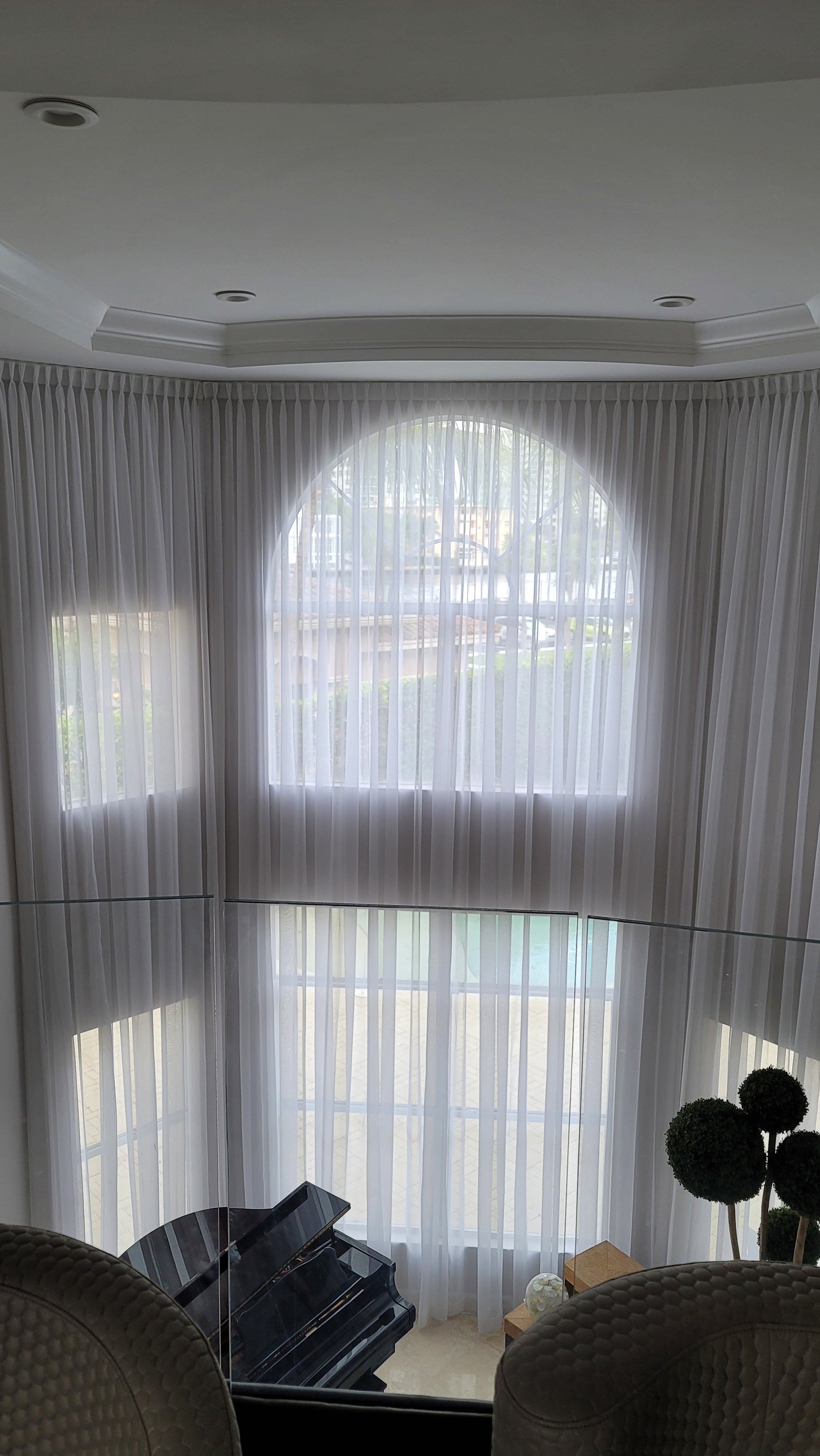 Living room with large arched window covered by sheer white pleated curtains.