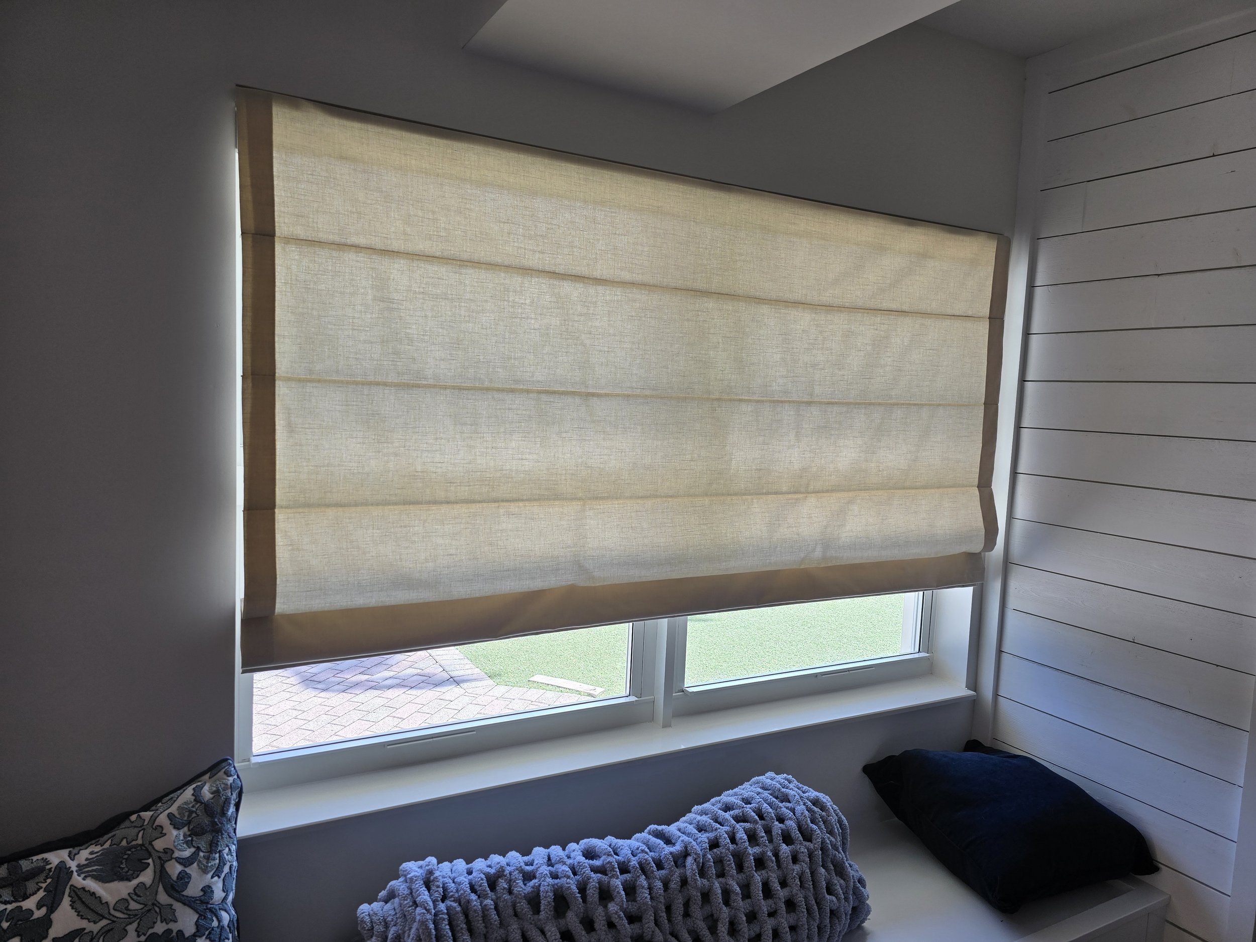 Indoor view of a window with beige flat Roman shade.