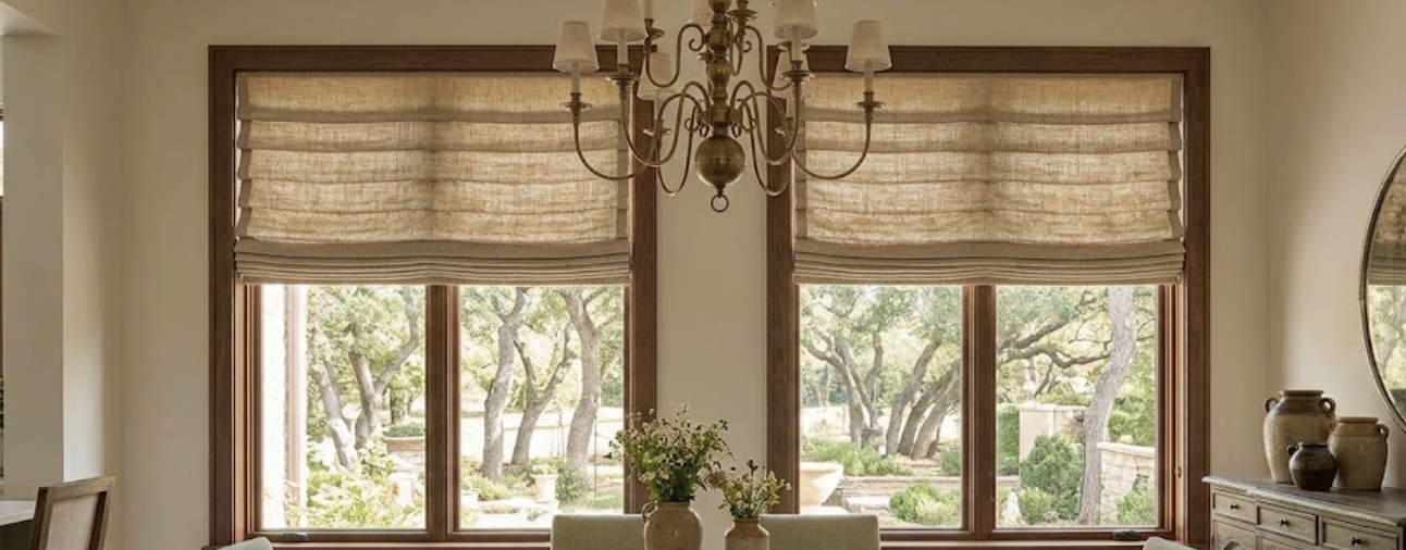 A room with large windows and beige hobbled Roman shades.