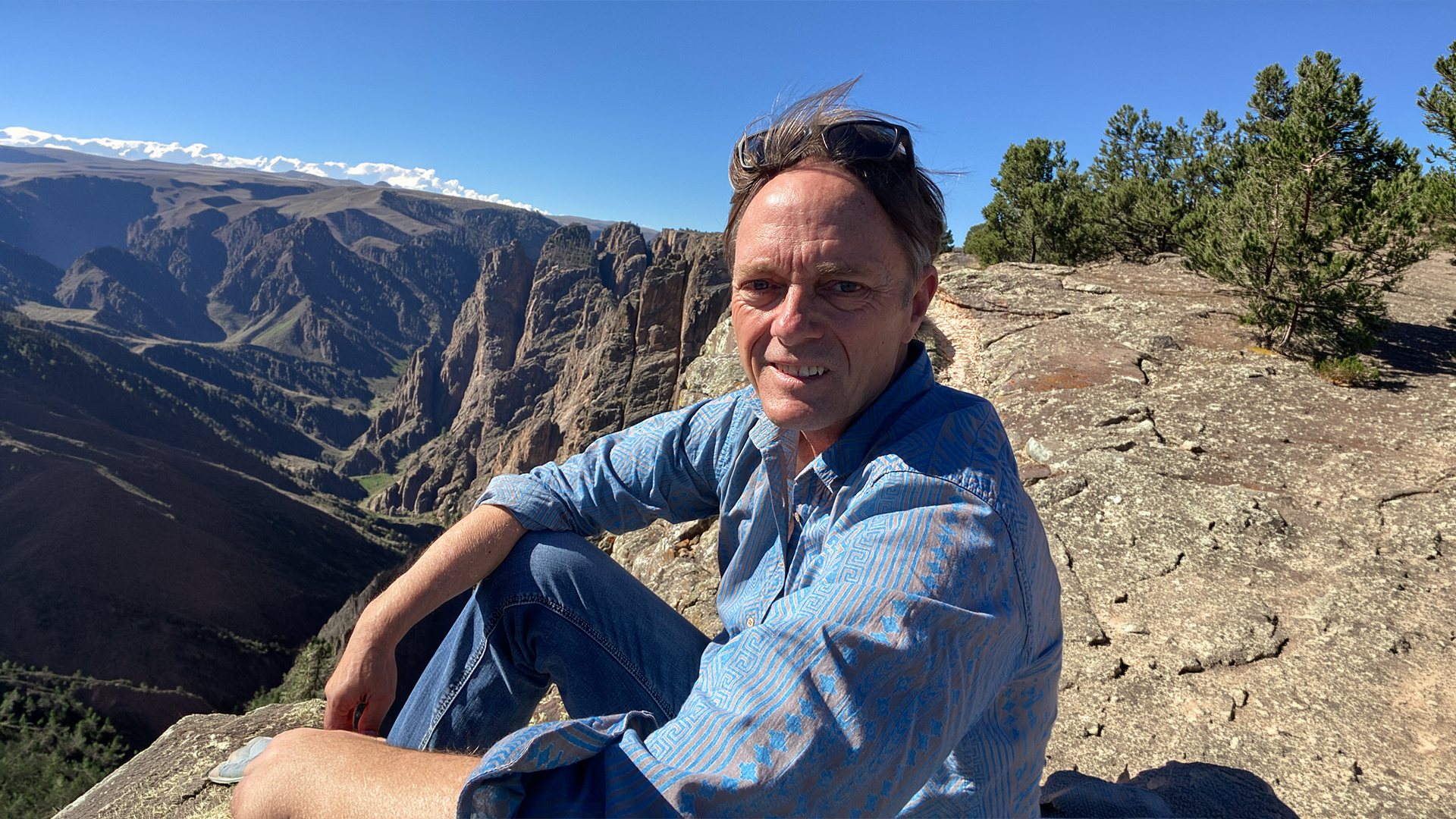 Traveler in a blue shirt sitting on a rocky overlook above a dramatic mountain canyon