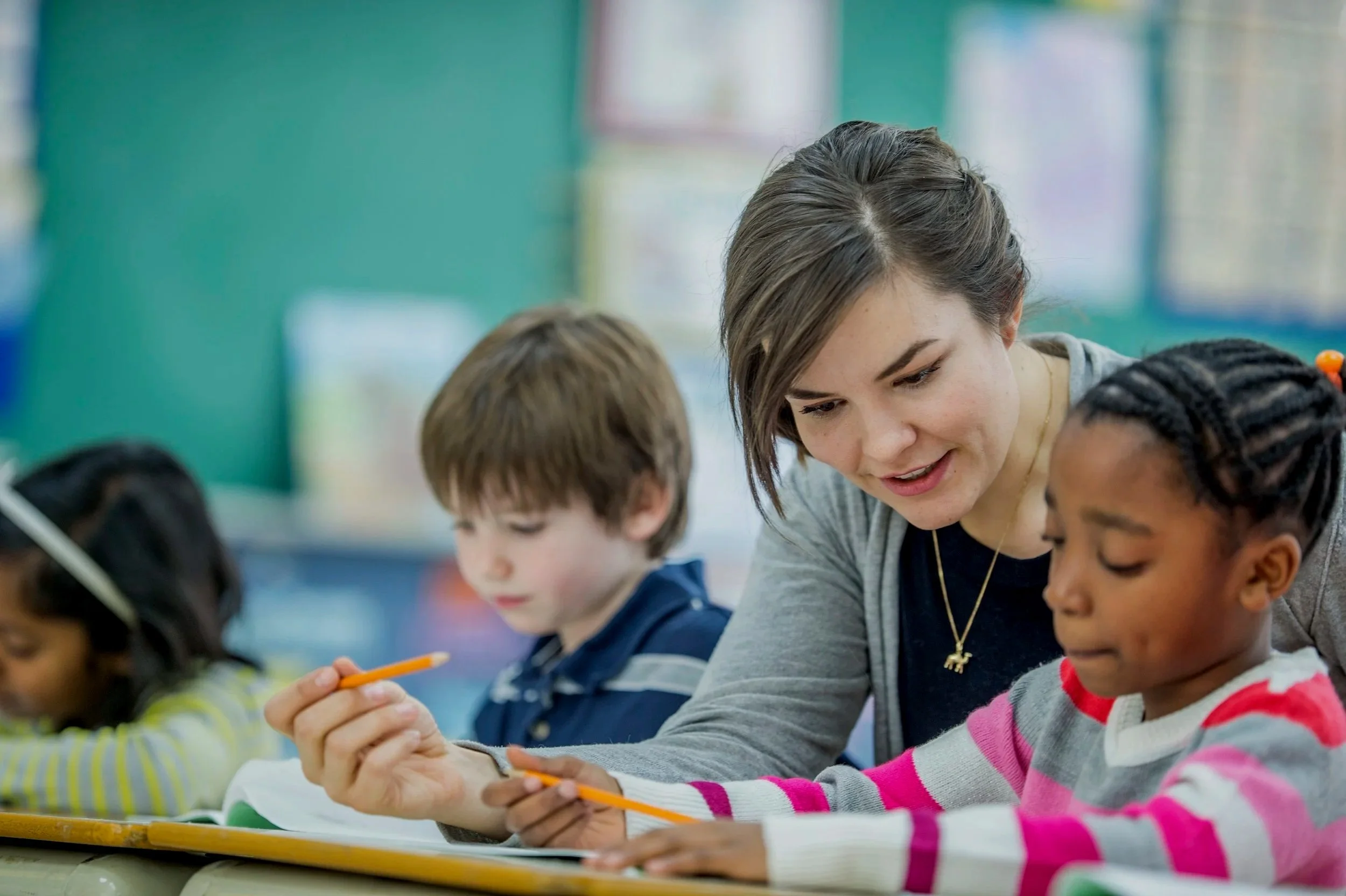 A teacher or adult helping children with their work in a classroom.