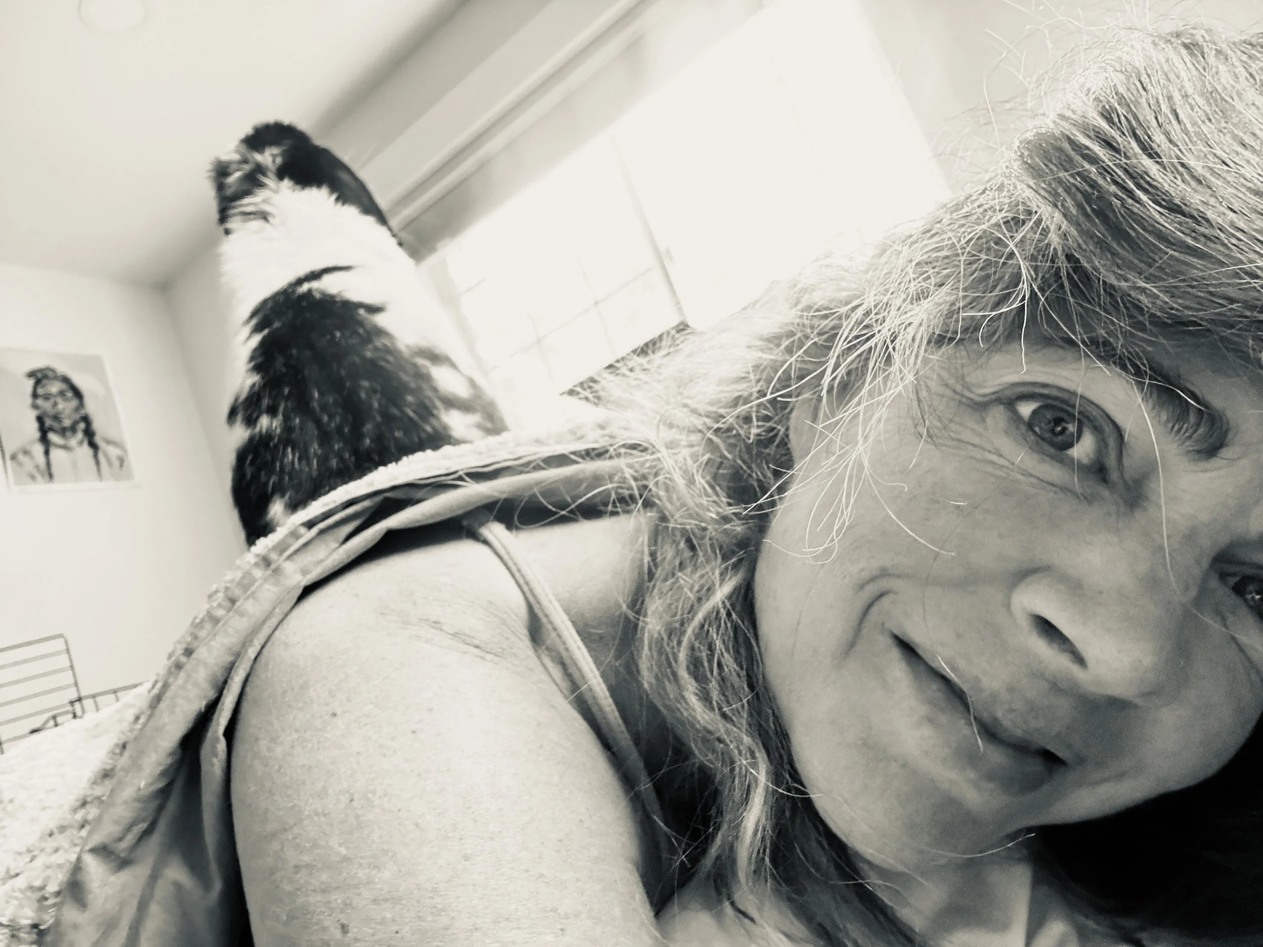A black and white photo of a person with long hair lying down and a cat sitting above them on the windowsill.