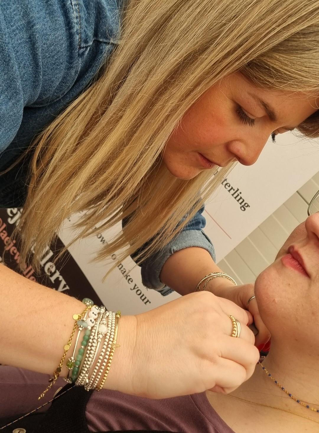 A woman with long blonde hair and bracelets doing the permanent jewellery experience at the mindful markets