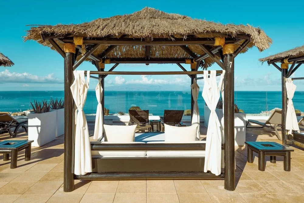 Luxe strandtent met uitzicht op de oceaan en ligbedden onder een heldere blauwe hemel.