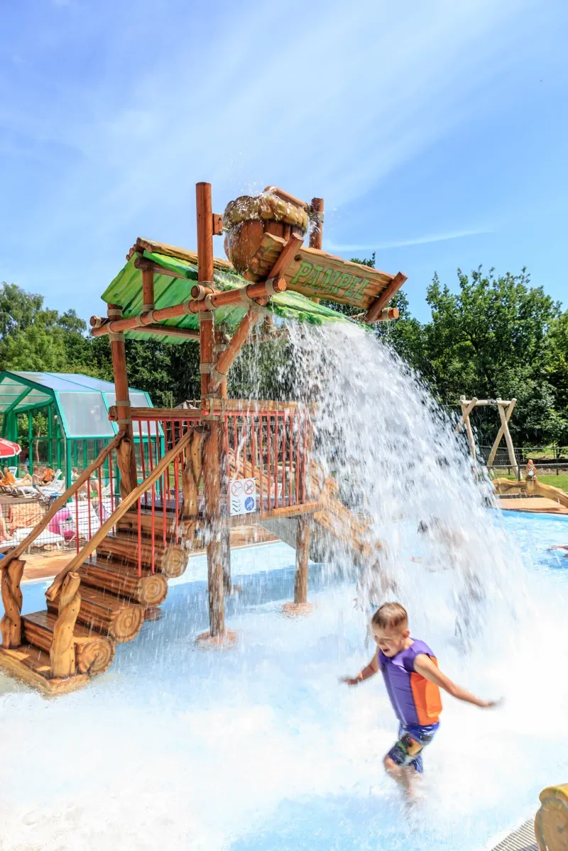Kind speelt onder een waterpomp op een waterpark.