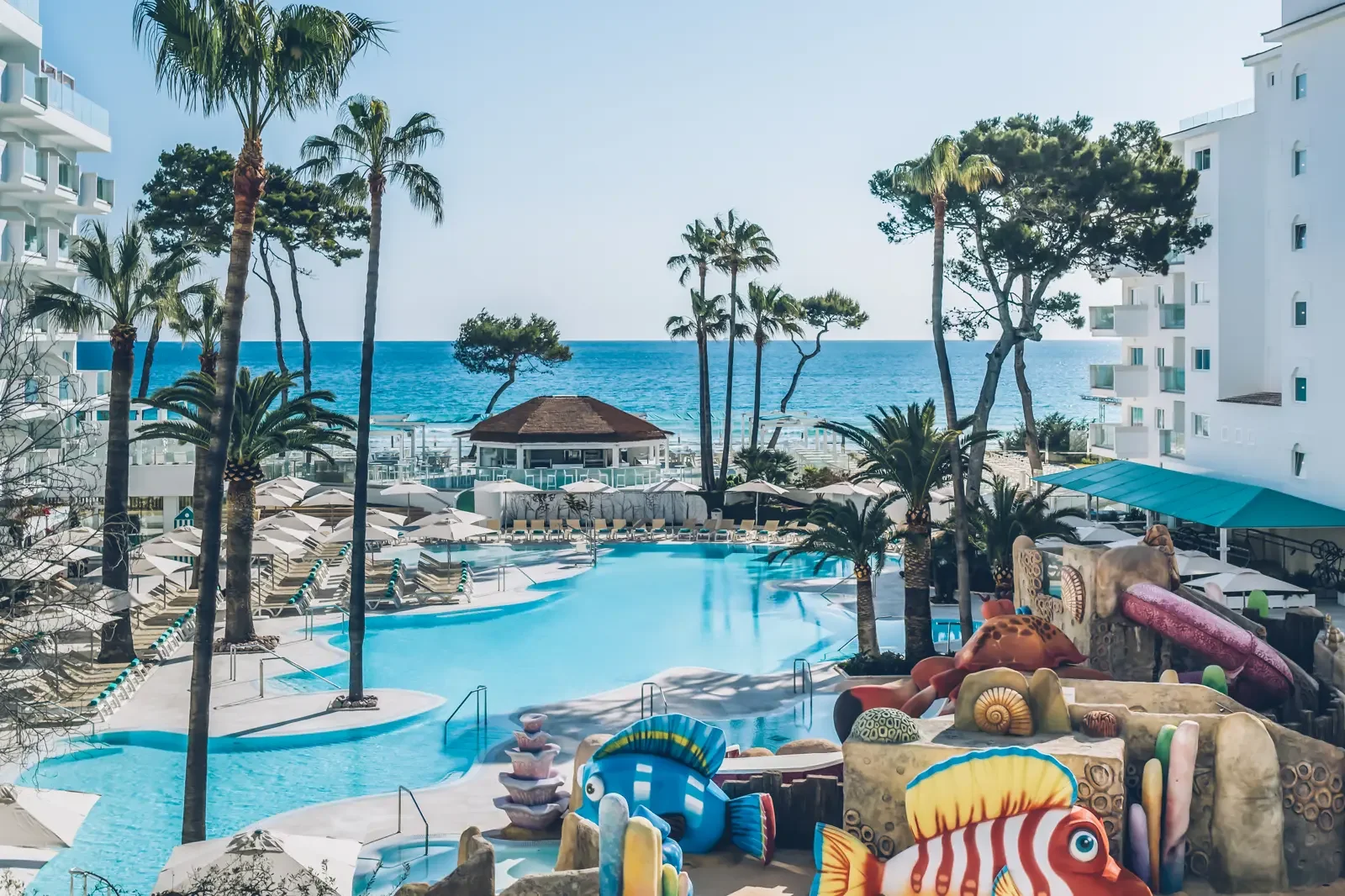 Uitzicht op een zwembad met ligbedden, parasols, palmbomen en een uitzicht op de oceaan vanuit een hotel of resort