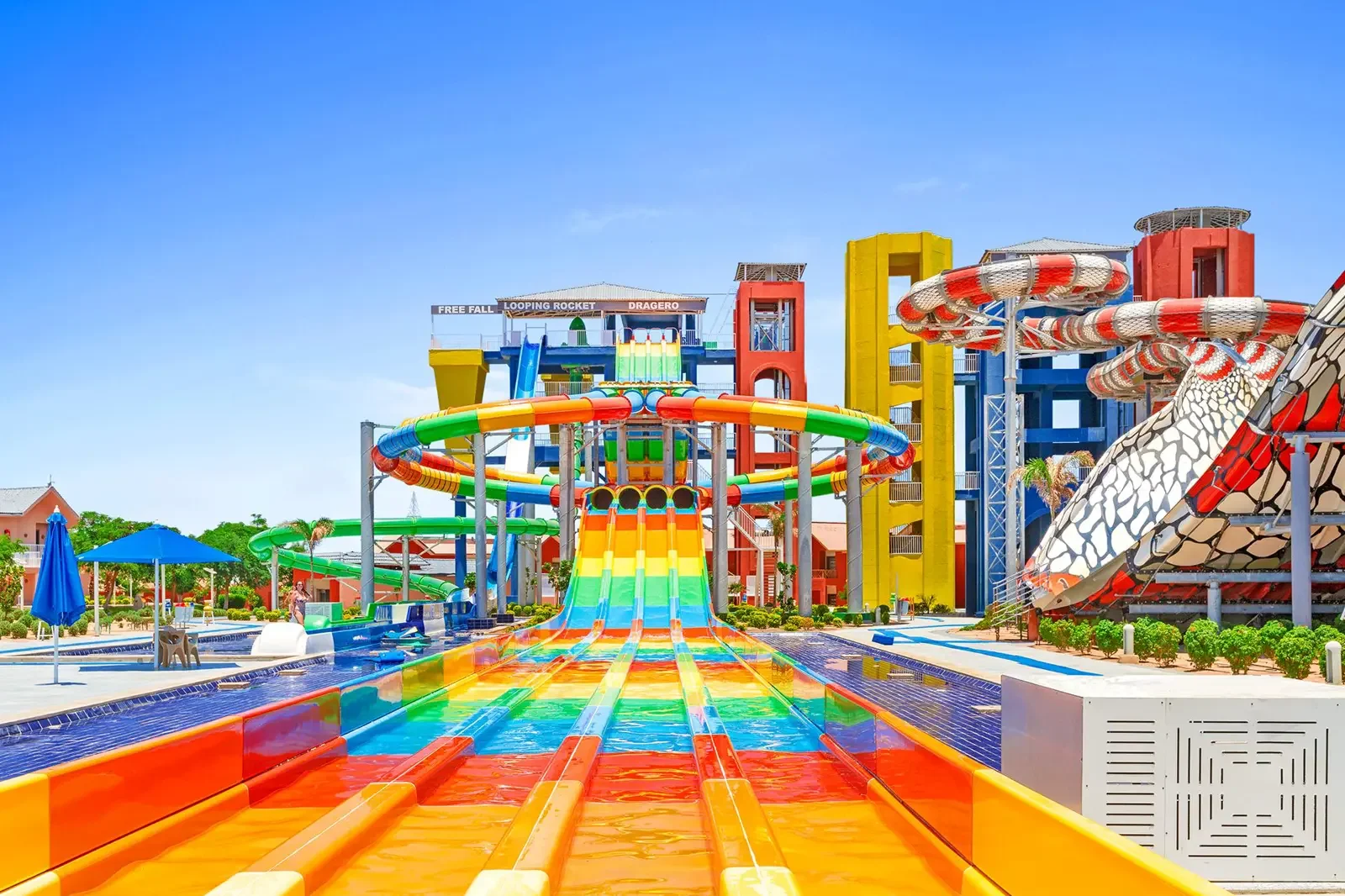 Colorrijk waterpark met meerdere glijbanen, waaronder een grote rainbow glijbaan en een spiraalvormige glijbaan, onder een blauwe hemel.