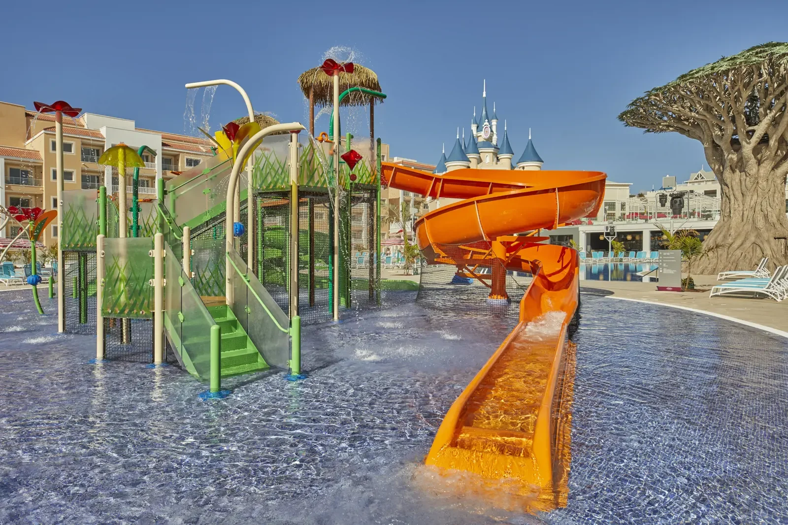 Waterglijbanen en speeltoestellen in een waterpark met kasteel op de achtergrond onder een blauwe hemel