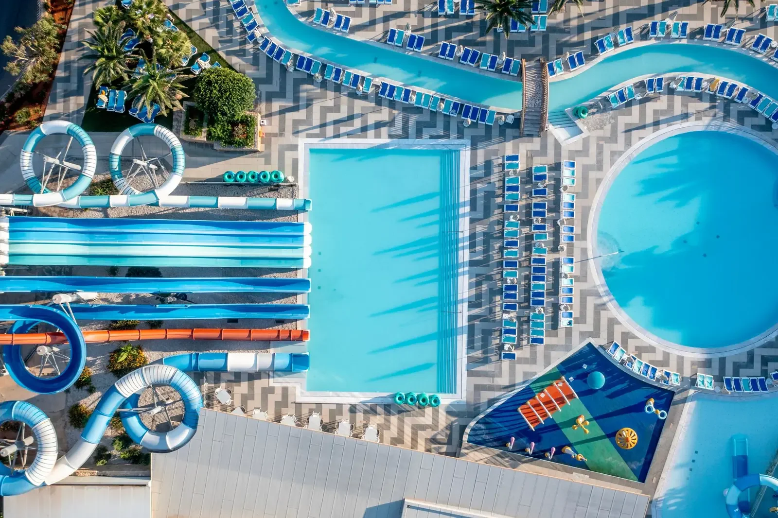 Uitzicht vanuit de lucht op een waterpark met meerdere zwembaden, glijbanen, ligstoelen en waterspeelplaatsen.