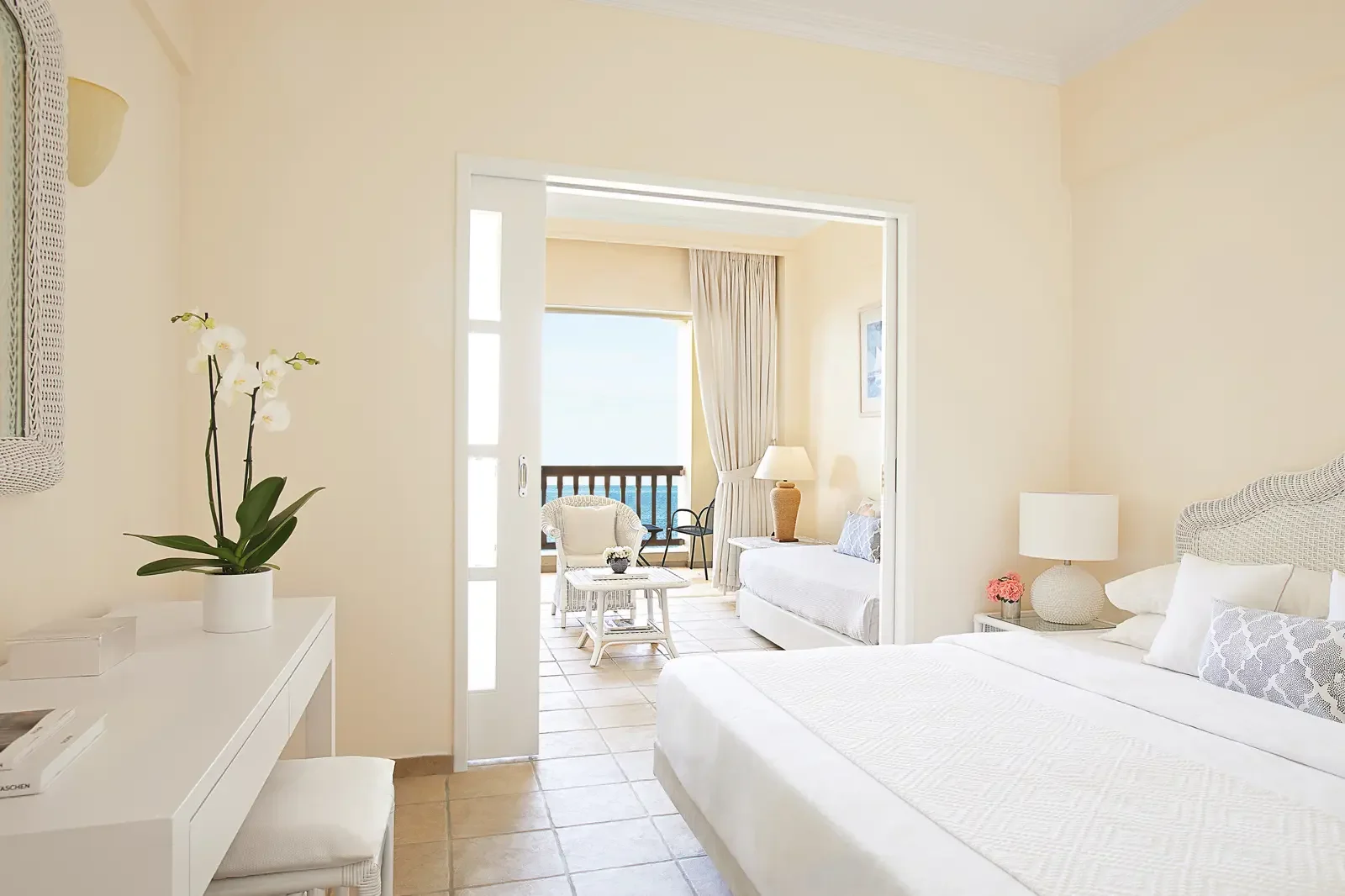 Lichte hotelkamer met witmeubels en uitzicht op een balkon met zee.
