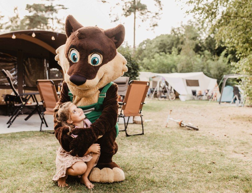Een meisje dat knuffelt met een grote mascotte van een hond in een campingachtergrond.