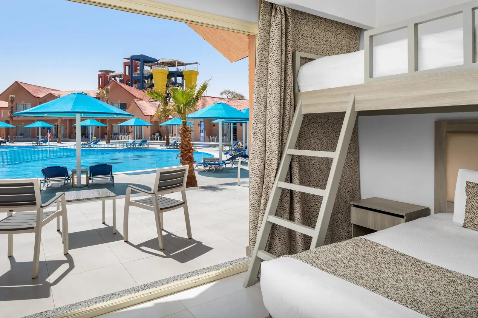 Kamerslaapkamer met stapelbed en uitzicht op zwembad met parasols en ligstoelen.